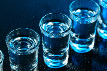 Wet glasses of vodka on dark blue background.