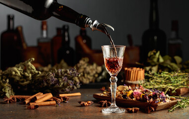 Brown herbal liquor or balm is poured from a vintage bottle into a glass.