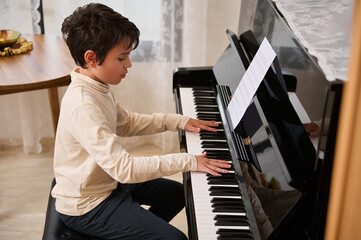 Adorable dark haired Latin American preteen child boy learning playing on chord instrument -...