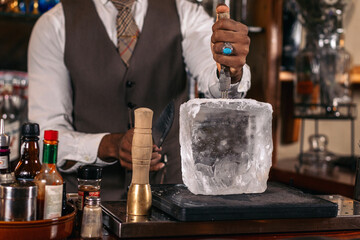 Close-up of an unrecognizable black bartender cutting a large ice cube to prepare a cocktail