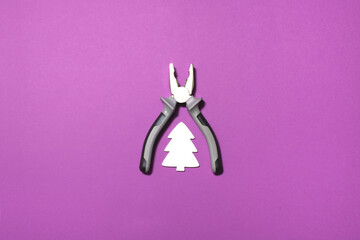 Combination pliers and white Christmas tree on a purple background with copy space. Minimal concept. Flat lay.