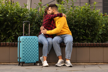 Long-distance relationship. Beautiful couple hugging on bench and suitcase outdoors