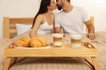 Obraz na płótnie Canvas Happy couple kissing on bed at home, focus on wooden tray with breakfast