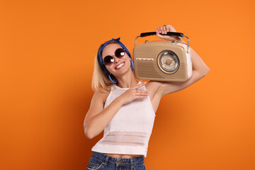 Happy hippie woman with retro radio receiver on orange background