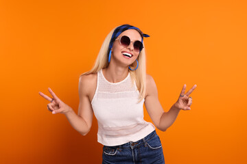 Smiling hippie woman showing peace signs on orange background