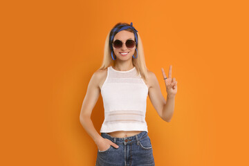 Smiling hippie woman showing peace sign on orange background