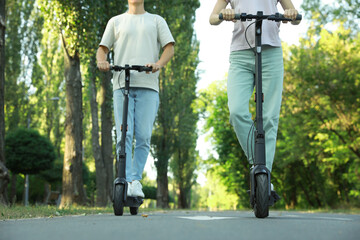 Couple riding modern electric kick scooters in park, closeup