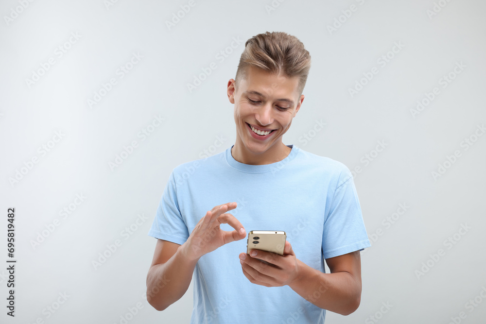 Poster Happy young man sending message via smartphone on light grey background