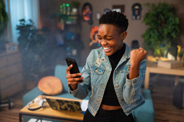 Happy african american teen girl lady woman with short hair using cell phone holding in hands...