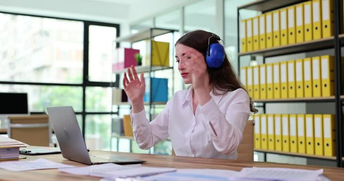 Woman Puts On Headphones And Works On Laptop In Office. Headphones With Active Noise Reduction For Noisy Office Concept