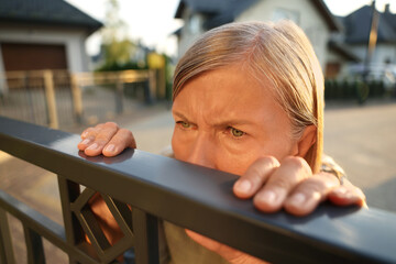 Concept of private life. Curious senior woman spying on neighbours over fence outdoors, closeup