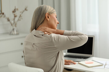 Woman suffering from neck pain at workplace in room - obrazy, fototapety, plakaty