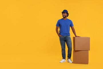 Happy courier with parcels on orange background, space for text - obrazy, fototapety, plakaty