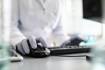 Close up shot of hands of laboratory specialist in medical gloves on computer mouse and keyboard on...