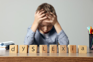 Little boy covering head with hands and cubes with word Dyslexia at wooden table, selective focus - obrazy, fototapety, plakaty