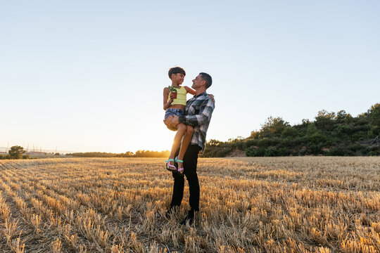 Loving father carries his daughter as they spend time together in the field.
