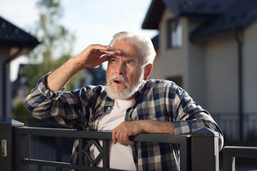 Concept of private life. Curious senior man spying on neighbours over fence outdoors
