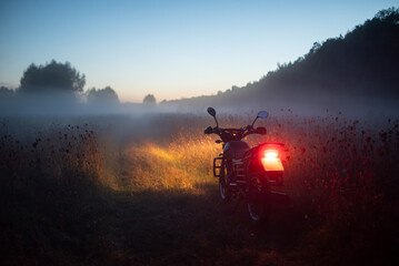 Motorcycle with its light on in the foggy field on a late evening. Bad visibility, driving...