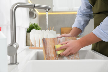 Man washing wooden cutting board in kitchen sink, closeup