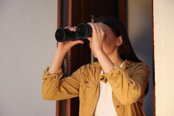 Concept of private life. Curious young woman with binoculars spying on neighbours outdoors