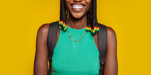 Close up portrait of a happy smiling young african american woman in green top, braids and backpack at studio isolated over yellow background. No face. - obrazy, fototapety, plakaty