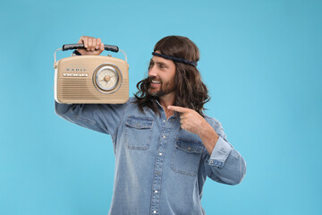 Stylish hippie man pointing at retro radio receiver on light blue background