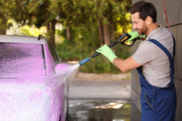 Worker washing auto with high pressure water jet at outdoor car wash