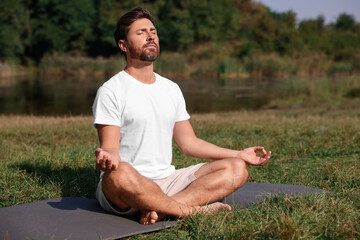 Naklejka na ściany i meble Man practicing yoga on mat outdoors. Lotus pose