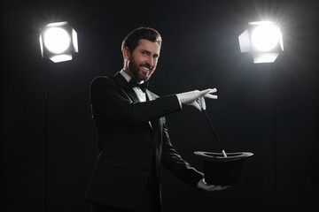 Happy magician showing magic trick with top hat on stage