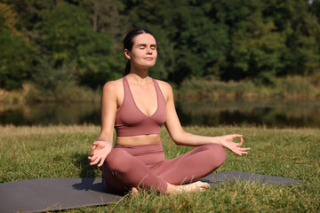 Naklejka na ściany i meble Beautiful woman practicing yoga on mat outdoors. Lotus pose