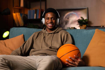 Basketball professional player sitting in the living room holding basketball ball in hand relaxing...