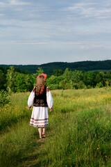 The girl, with her back turned and dressed in Ukrainian national clothes, walks barefoot in the field.