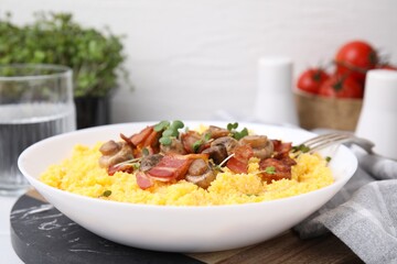 Tasty cornmeal with bacon, mushrooms and microgreens in bowl on table, closeup