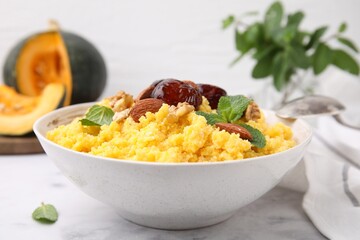 Tasty cornmeal with dates, nuts and mint in bowl on white marble table, closeup
