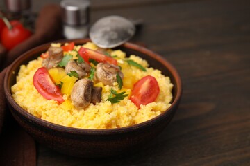 Tasty cornmeal with tomatoes, pepper and mushrooms in bowl on wooden table, closeup. Space for text