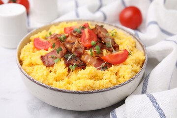 Tasty cornmeal with tomatoes, bacon and microgreens in bowl on white table, closeup