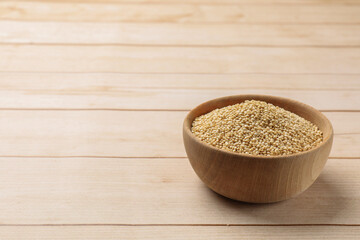 Raw quinoa in bowl on wooden table, space for text