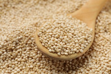 Wooden spoon and raw quinoa as background, closeup