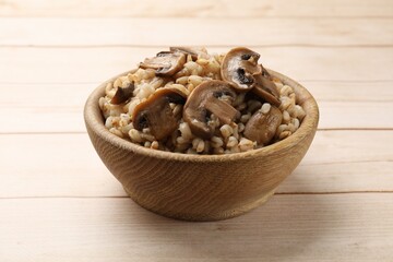 Delicious pearl barley with mushrooms in bowl on wooden table, closeup