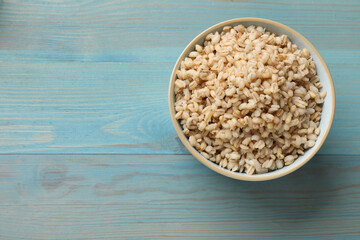 Delicious pearl barley in bowl on light blue wooden table, top view. Space for text