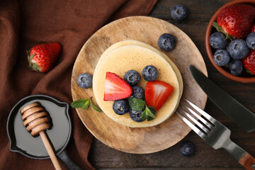 Delicious pancakes with strawberries, blueberries and mint served on wooden table, flat lay