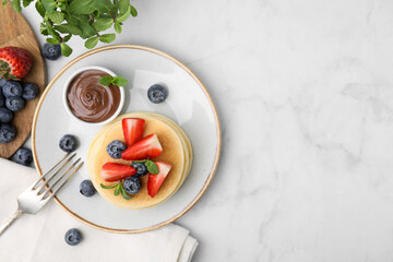Delicious pancakes with strawberries, blueberries, mint and chocolate sauce served on light marble table, flat lay. Space for text - obrazy, fototapety, plakaty
