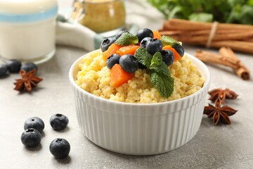 Tasty millet porridge with blueberries, pumpkin and mint in bowl on light grey table, closeup