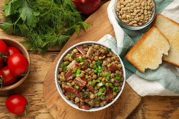 Delicious lentils with bacon and green onion in bowl served on wooden table, flat lay