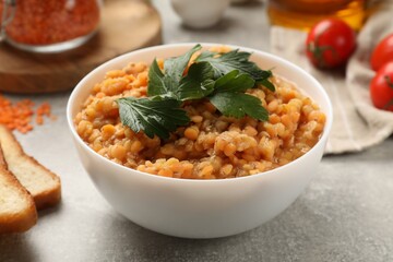 Delicious red lentils with parsley in bowl on light grey table, closeup