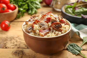 Tasty quinoa porridge with fried bacon and mushrooms in bowl on wooden table, closeup