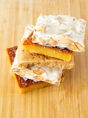 Turron blocks with almonds and hazelnuts on chopping board, on wooden table.
