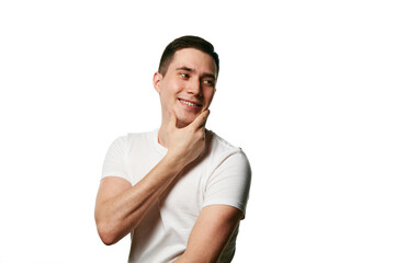 Attractive man, well-groomed guy in T-shirt smiling and touching chin looking away against white background. Concept of beauty treatment and hygiene, self-care, anti-aging procedures. Copy space. Ad