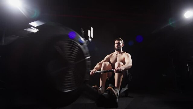 Young strong bearded bodybuilder doing a low row of rope pulleys while sitting. fitness male athlete training rowing machine exercise intense endurance training.