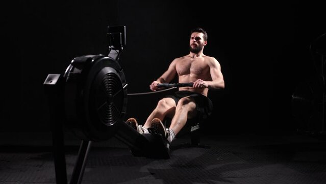 Young strong bearded bodybuilder doing a low row of rope pulleys while sitting. fitness male athlete training rowing machine exercise intense endurance training.